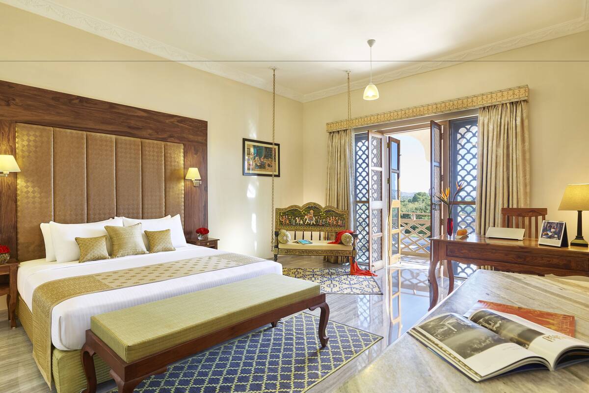A hotel room with a large bed, a bench, a desk, and a view of the outdoors.