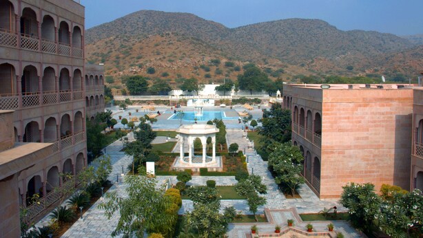A courtyard with a central fountain, surrounded by arched walkways and lush greenery, set against a backdrop of hills. - Pratap Mahal, Ajmer - IHCL SeleQtions (Pushkar)