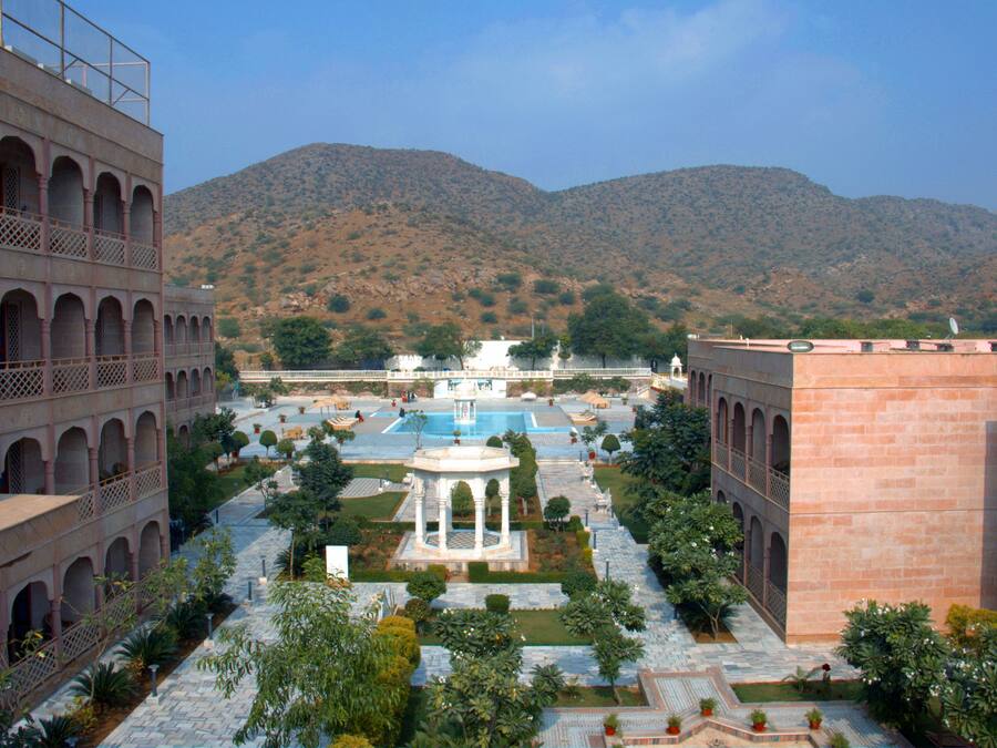A courtyard with a central fountain, surrounded by arched walkways and lush greenery, set against a backdrop of hills.