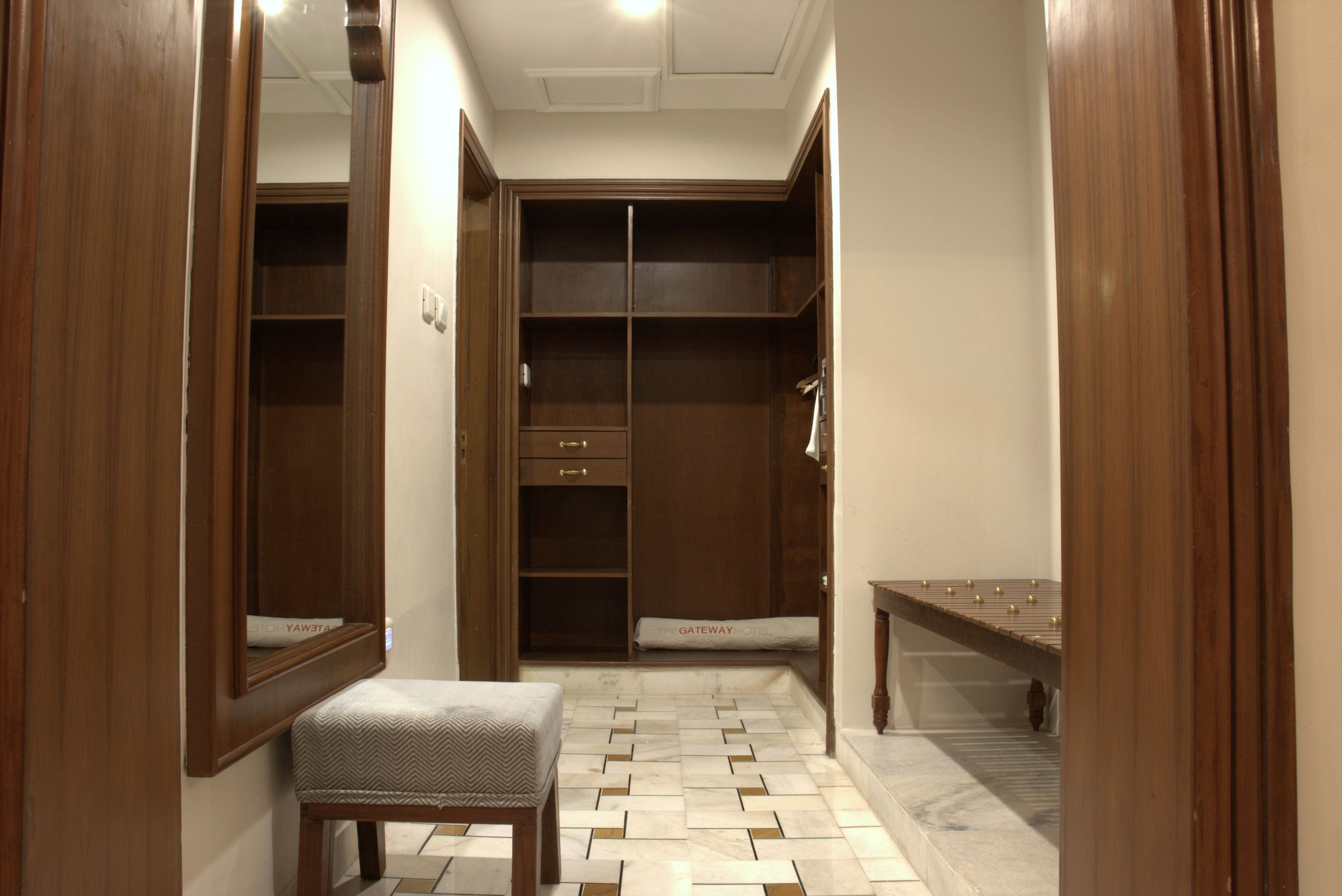 Habitación de hotel con un armario de madera, un banco y piso de baldosas.