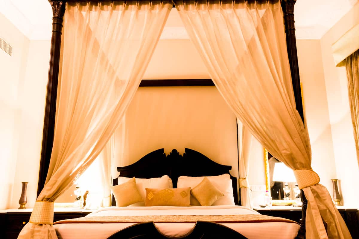 A four-poster canopy bed with a dark headboard, white linens, and multiple pillows.