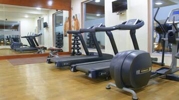 Un gimnasio con cintas de correr, bicicletas estáticas y un espejo grande.