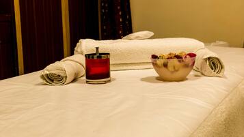 A neatly made bed with a rolled towel, a glass of red beverage, and a bowl of fruit on a hotel room bed.