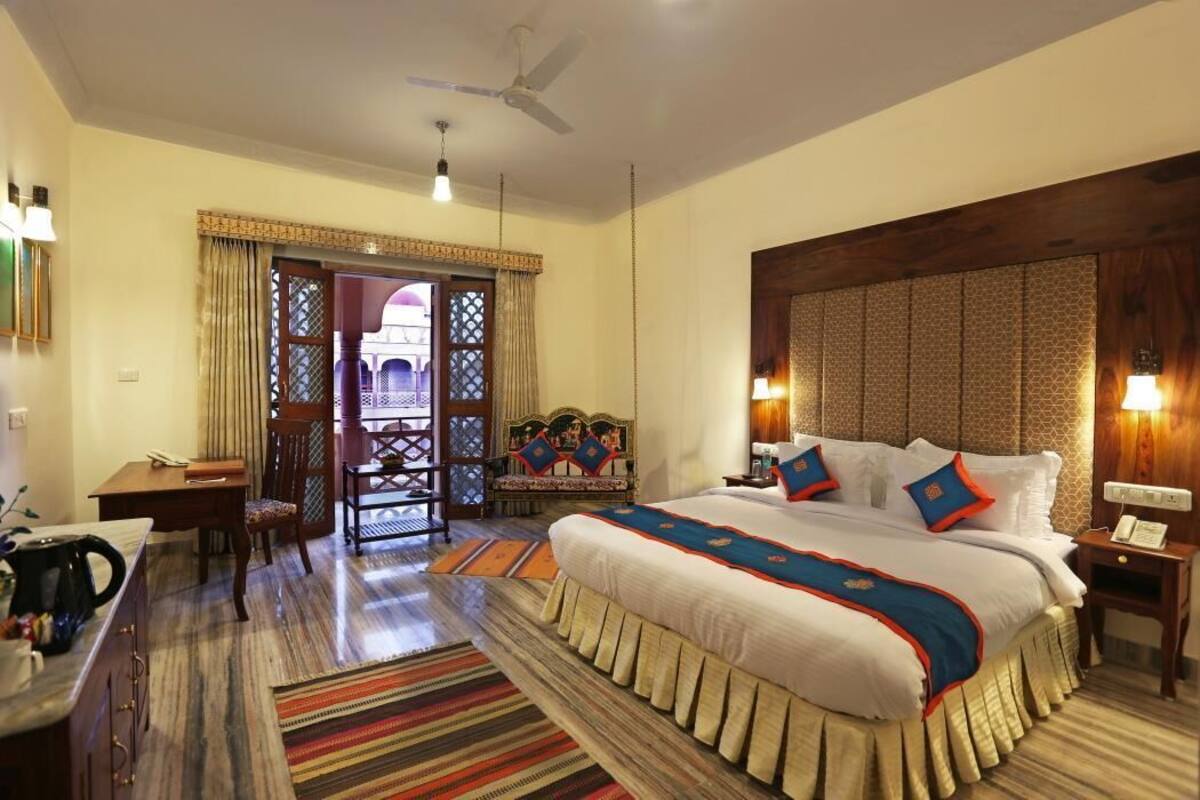 A hotel room with a large bed, a desk, a chair, a dining table, and a view through a door.