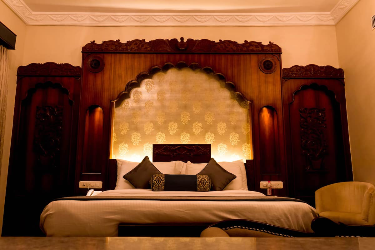 A hotel room with a large bed, ornate headboard, and a chair.