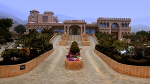 A grand building with a central staircase leading to an entrance, surrounded by well-maintained gardens and a clear sky. - Pratap Mahal, Ajmer - IHCL SeleQtions (Pushkar)