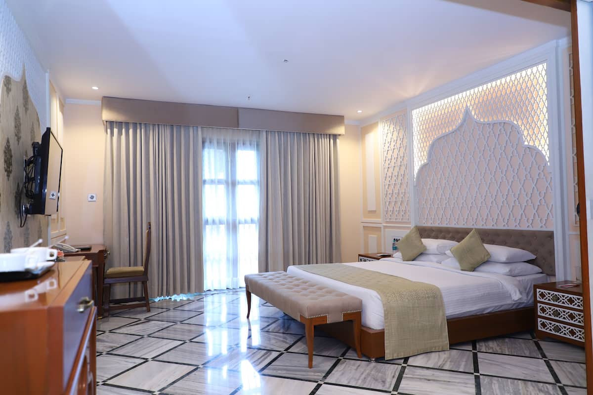 A hotel room with a large bed, a wooden bench, a desk, and a TV.