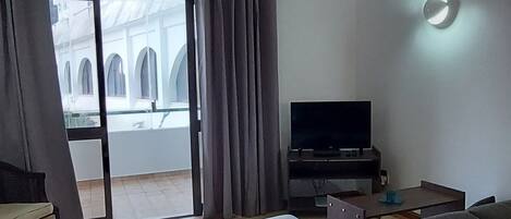 A modern living room with a sofa, a flat-screen TV, and a balcony with curtains.