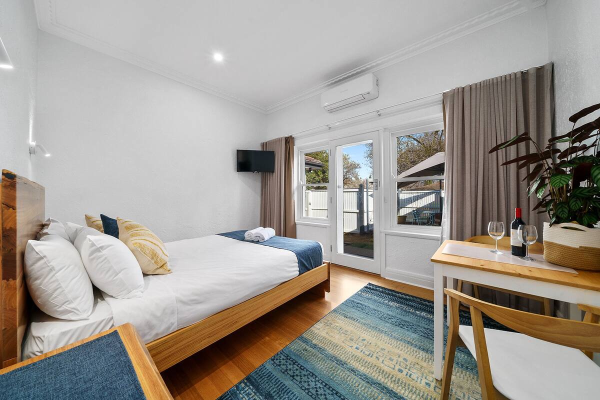 Un dormitorio con cama, escritorio con silla, televisor y ventana con cortinas.