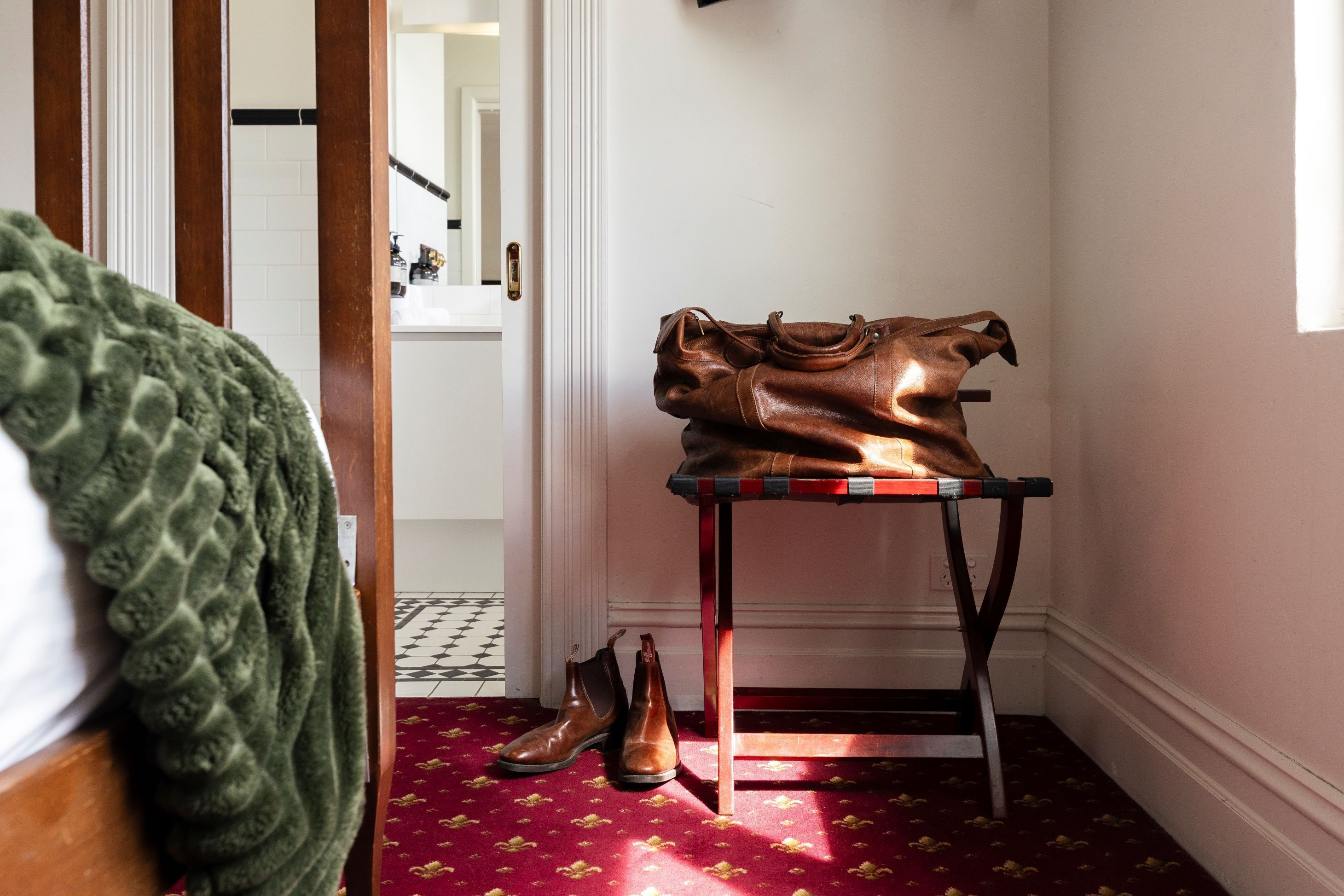 Una habitación con una silla de madera, una mesa con un bolso de cuero marrón, y un par de zapatos marrones en el suelo.