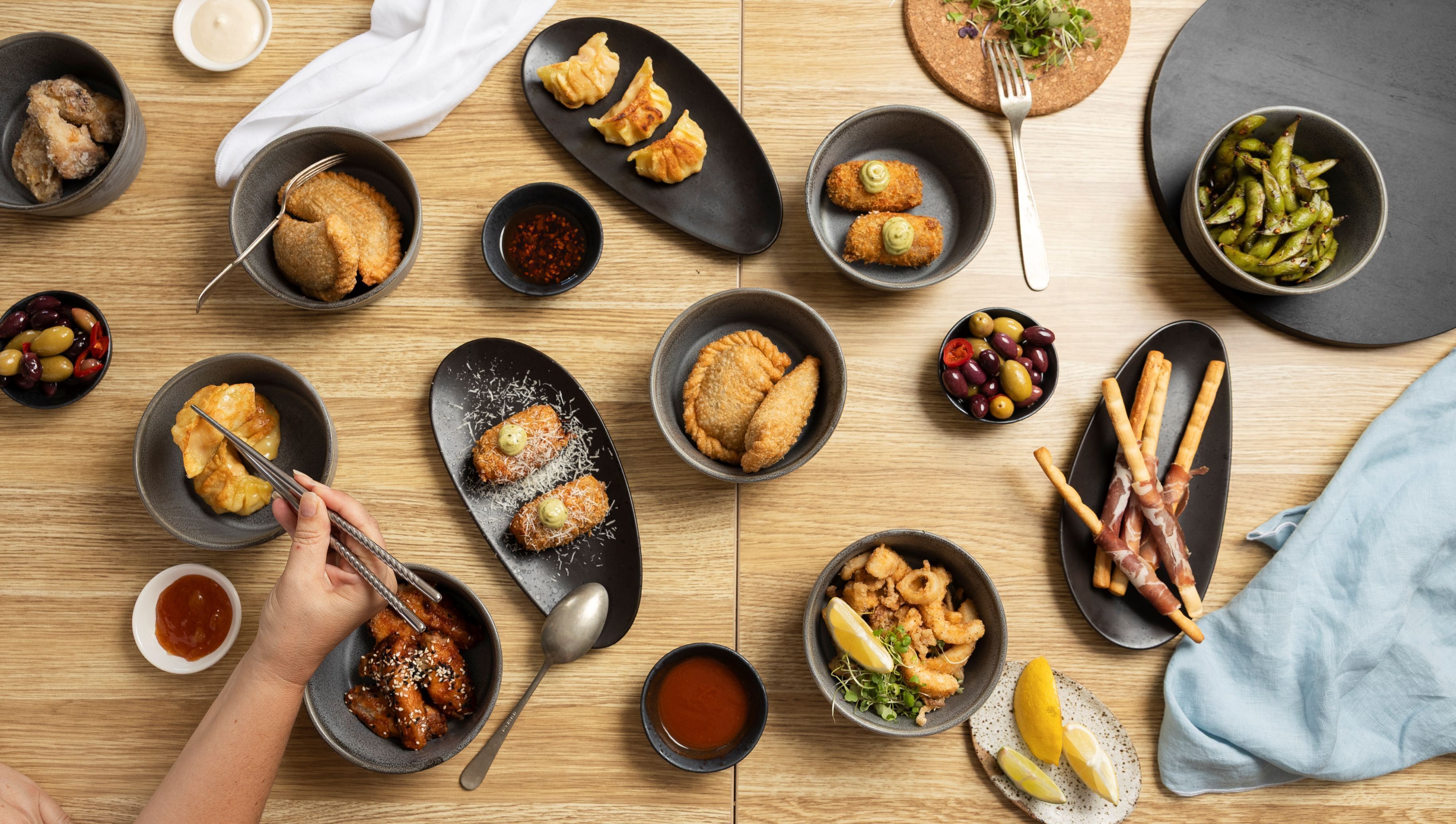 Une variété de plats sont disposés sur une table en bois, notamment des aliments frits, des olives et un bol de sauce.