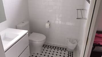 Un baño pequeño y limpio con azulejos blancos, un inodoro, un lavamanos y una zona de ducha.