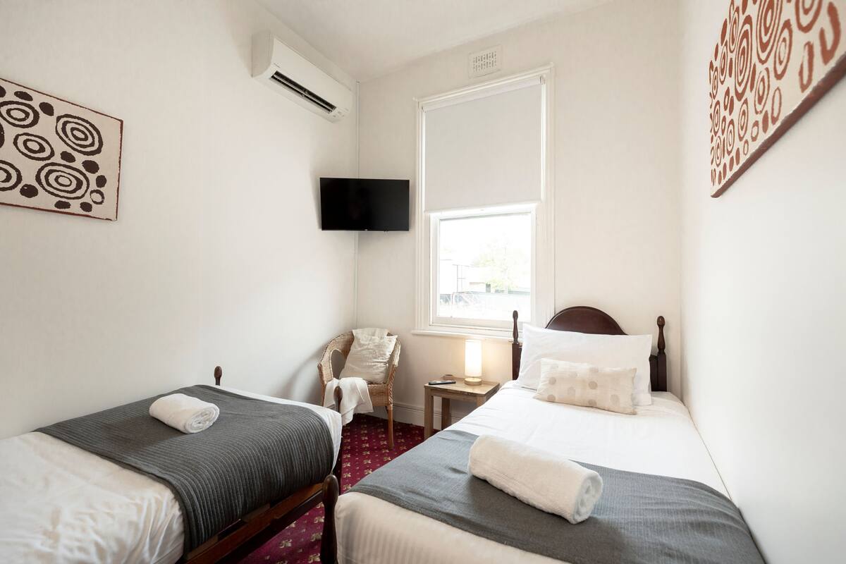 Une chambre d’hôtel avec deux lits, une chaise, une télévision et une fenêtre.