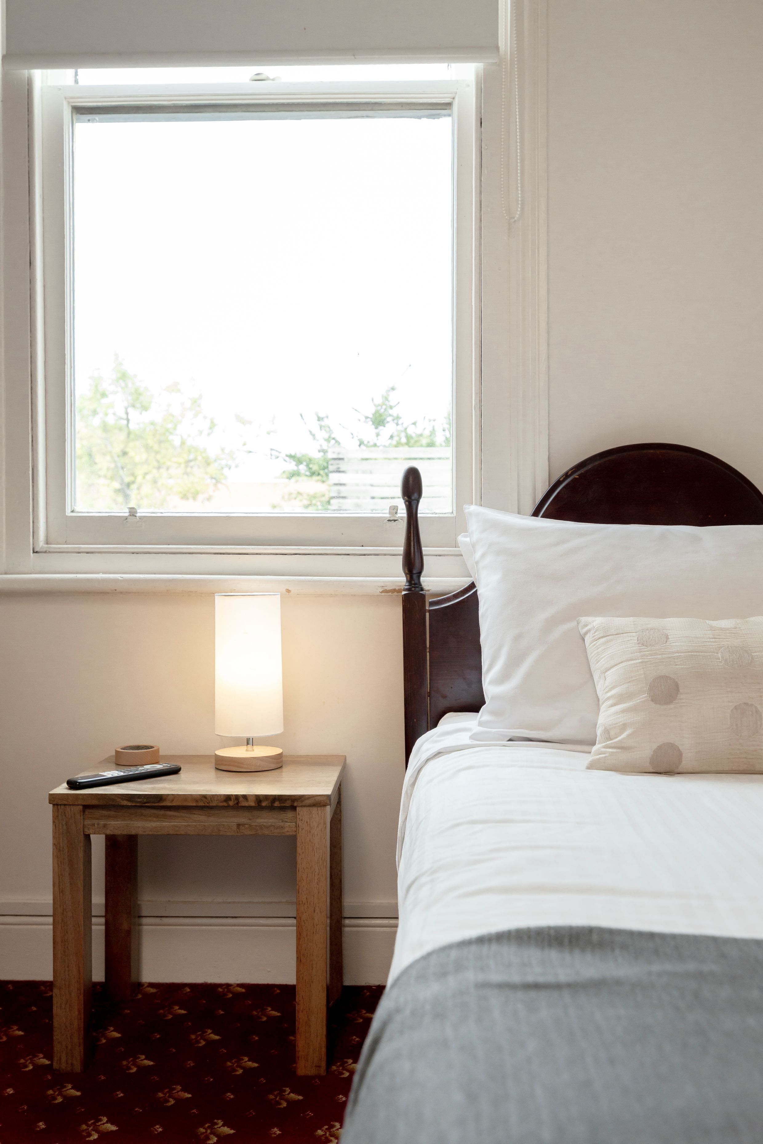 A bedroom with a bed, a nightstand with a lamp, a window, and a view of trees outside.
