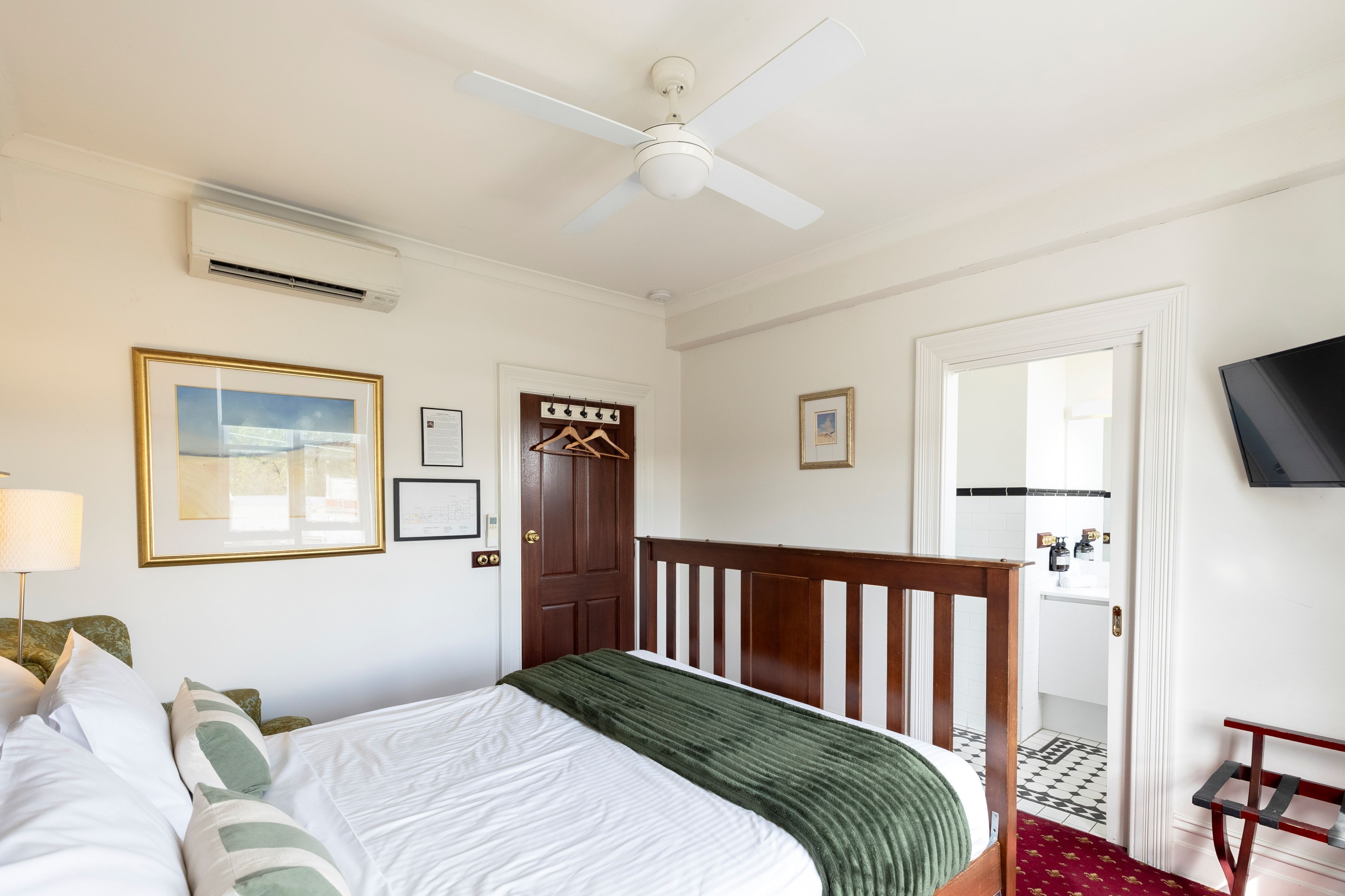 A bedroom with a bed, a ceiling fan, a door, and a television on the wall.