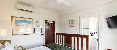 A bedroom with a bed, a ceiling fan, a door, and a television on the wall.