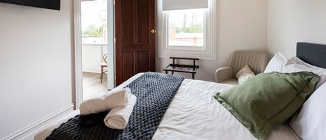 Un dormitorio con cama, una silla, un ventanal y una puerta.