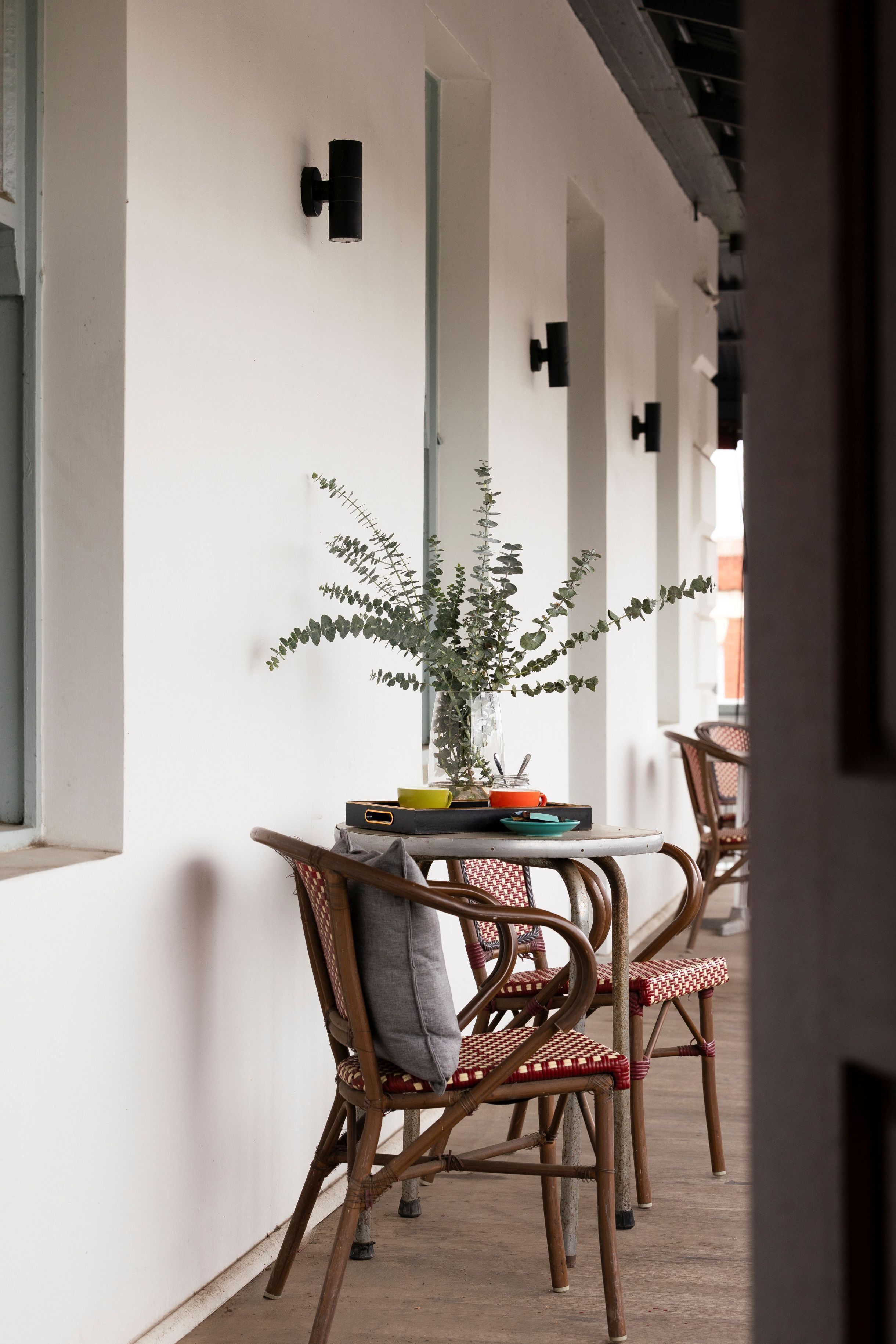 A corridor with wicker chairs, a table with a plant, and a window.