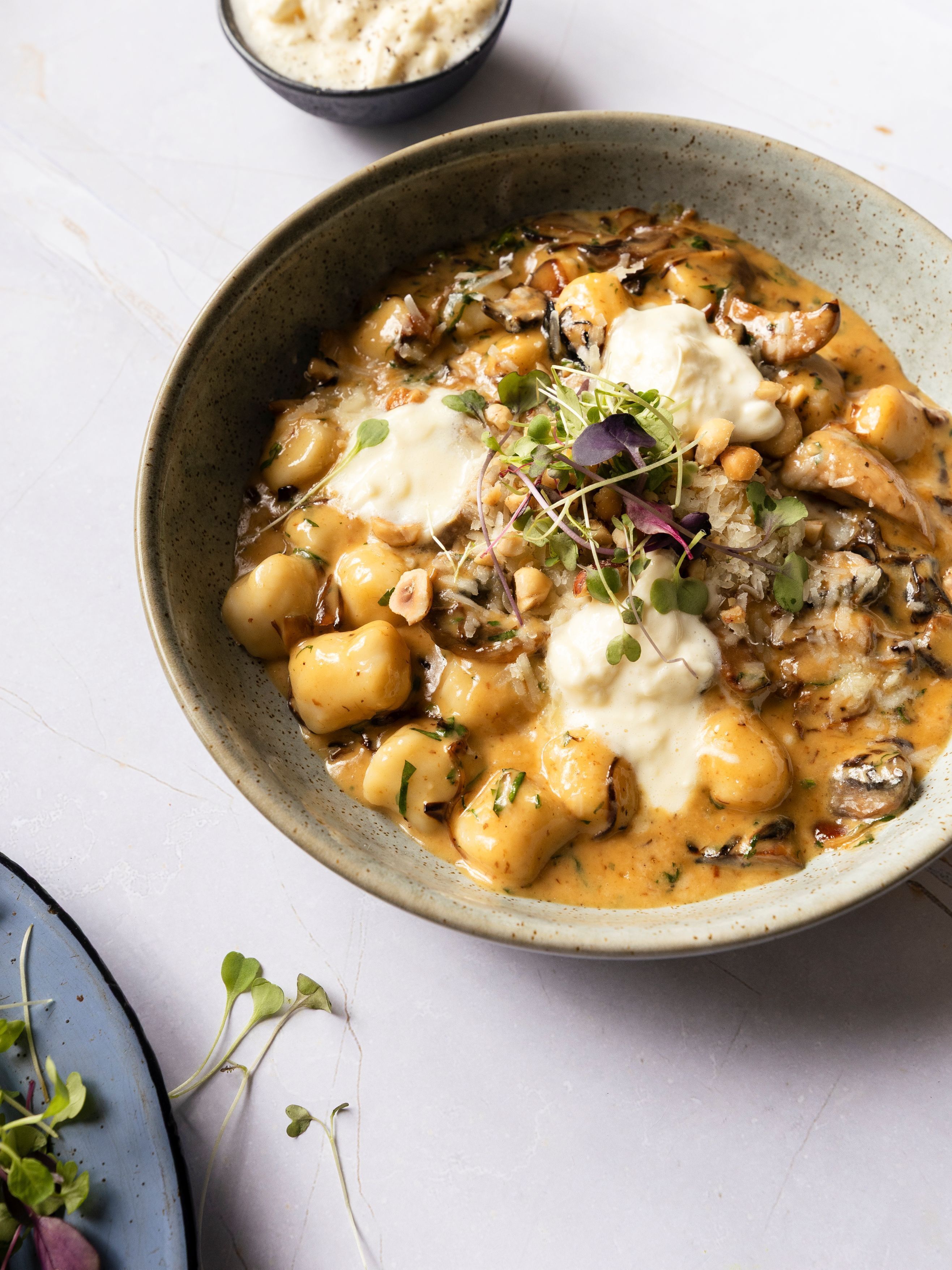 A bowl of food with a creamy sauce, garnished with herbs and sprouts.