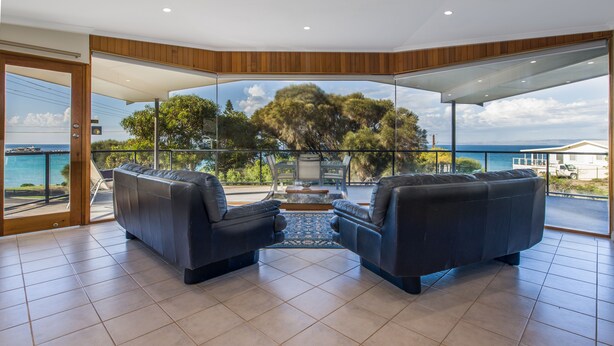 A modern living room with a glass wall offering a scenic view of the sea and trees. - Baudin House (Penneshaw)