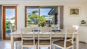 A dining area with a white table and chairs, a glass door leading to a balcony, and a framed picture on the wall. - Baudin House (Penneshaw)