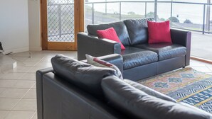 A living room with a dark leather sofa, a patterned rug, and a view of a body of water through large windows. - Baudin House (Penneshaw)