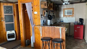 A rustic kitchen with wooden walls, a bar area with stools, a red refrigerator, and a chalkboard with a message. - Roundtop Mountain Vista - Cabins and Motel (Thermopolis)
