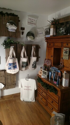 Interior rústico de una cabaña con paredes de madera, un aparador de madera y diversos objetos como bolsos, una mesa con mantel blanco y un cartel que dice "WELCOME TO OUR CABIN".