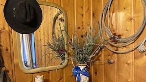 A wooden dresser with a mirror, a black hat, a vase with plants, and a rope coiled on the wall. - Roundtop Mountain Vista - Cabins and Motel (Thermopolis)