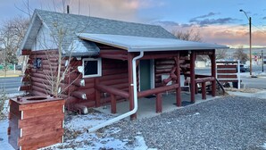 A rustic log cabin with a covered porch and a small window. - Roundtop Mountain Vista - Cabins and Motel (Thermopolis)