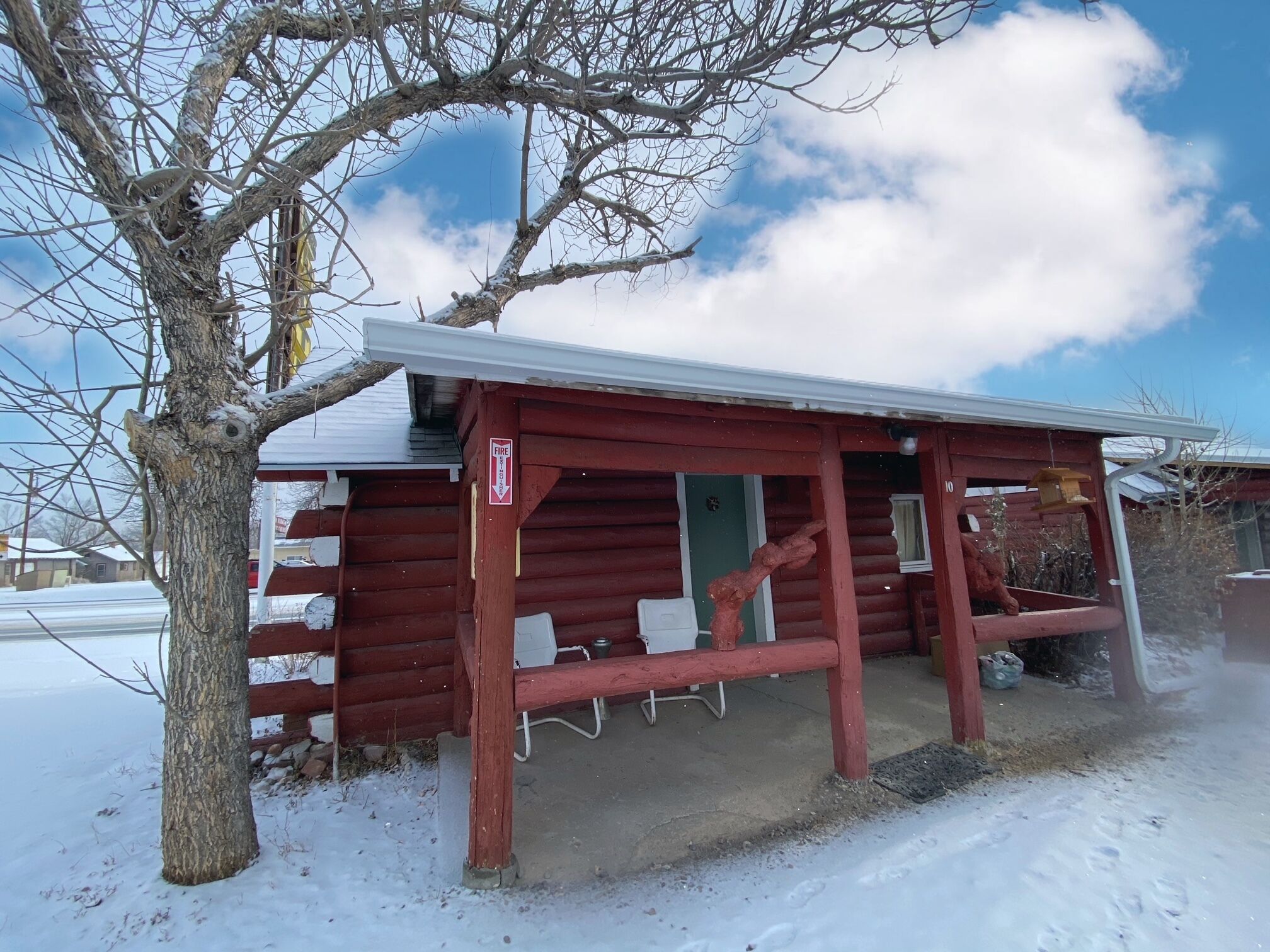 A red wooden cabin with a snow-covered ground, a bench, and a fire hydrant outside.