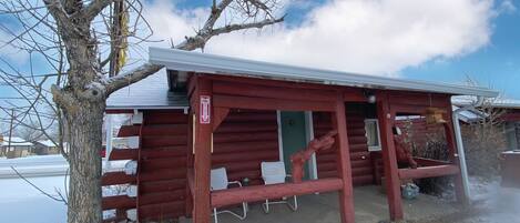 A red wooden cabin with a snow-covered ground, a bench, and a fire hydrant outside.