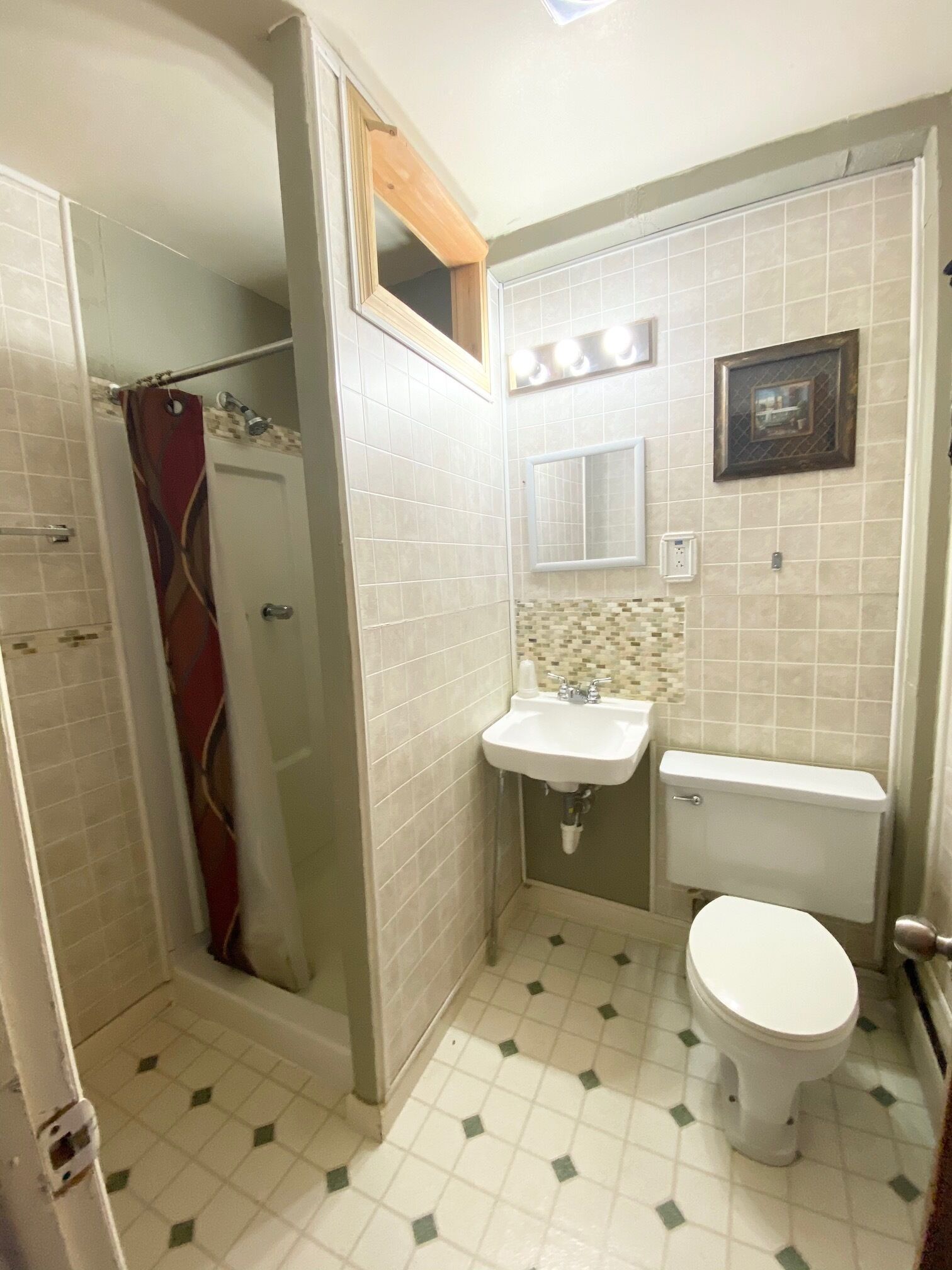 A bathroom with a shower, toilet, sink, and a mirror.