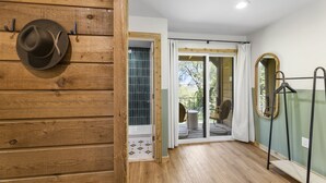 A room with wooden paneling, a hat on the wall, a sliding glass door leading to an outdoor area, and a mirror on the wall.