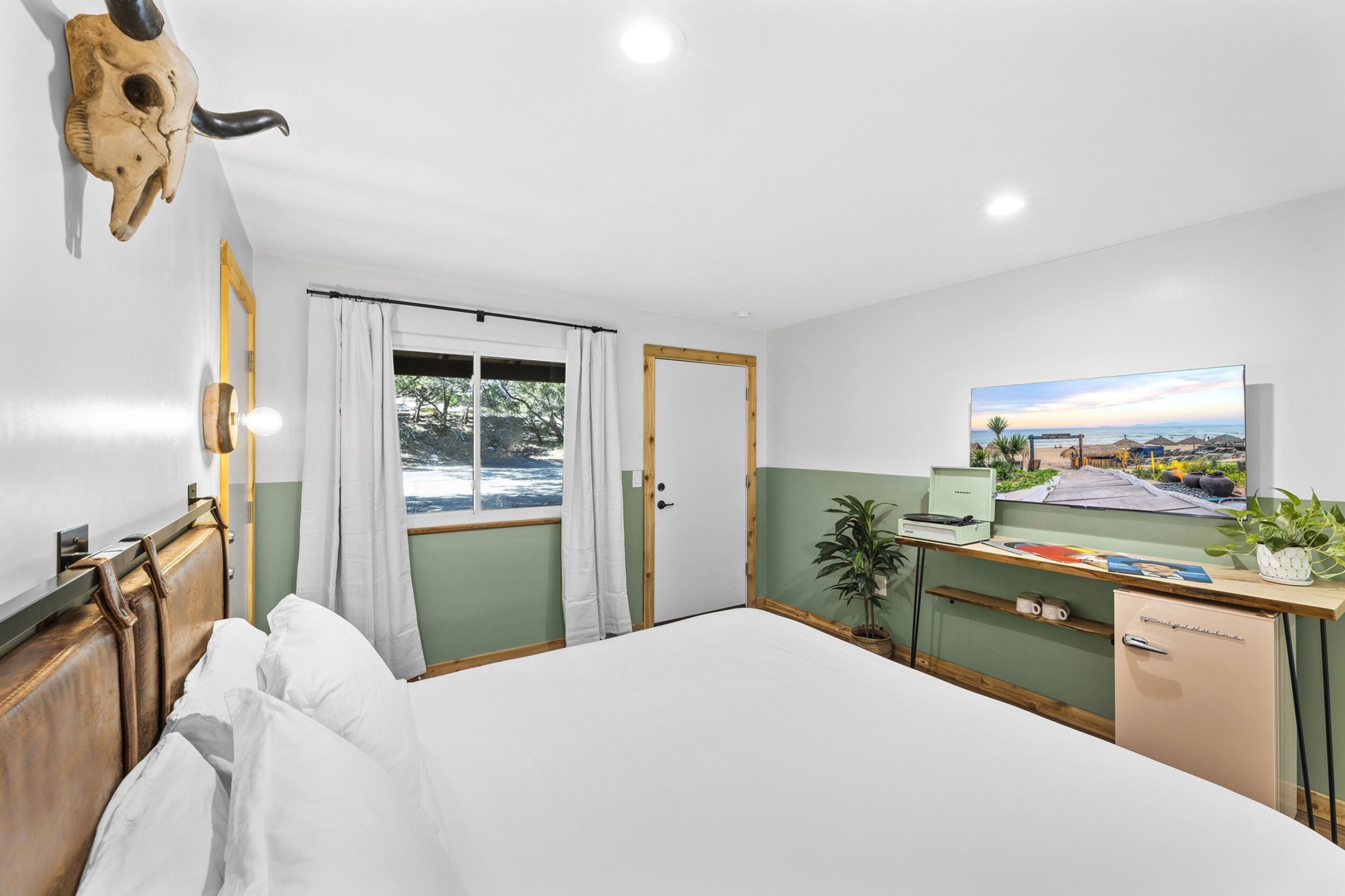 Ein Schlafzimmer mit einem Bett, einem Schreibtisch, einer Zimmerpflanze, einem Spiegel und einem Bild an der Wand.