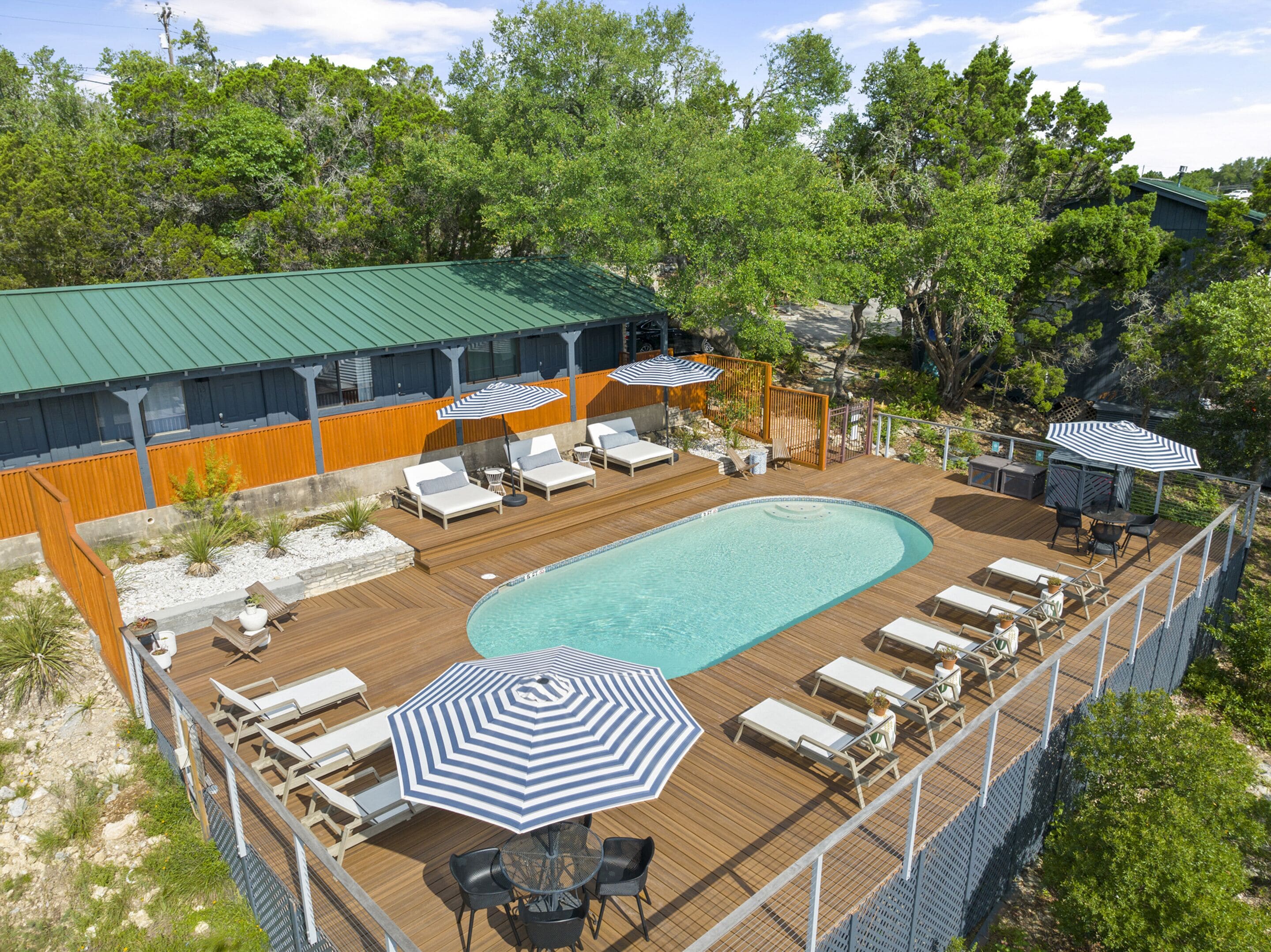 A rooftop pool area with lounge chairs, umbrellas, and a wooden deck.