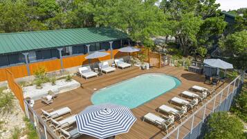 A rooftop pool area with lounge chairs, umbrellas, and a wooden deck.
