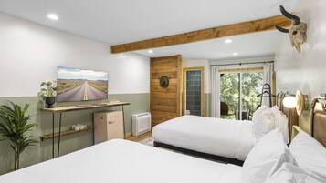 A bedroom with two beds, a TV, a desk, a plant, and a wooden ceiling beam.