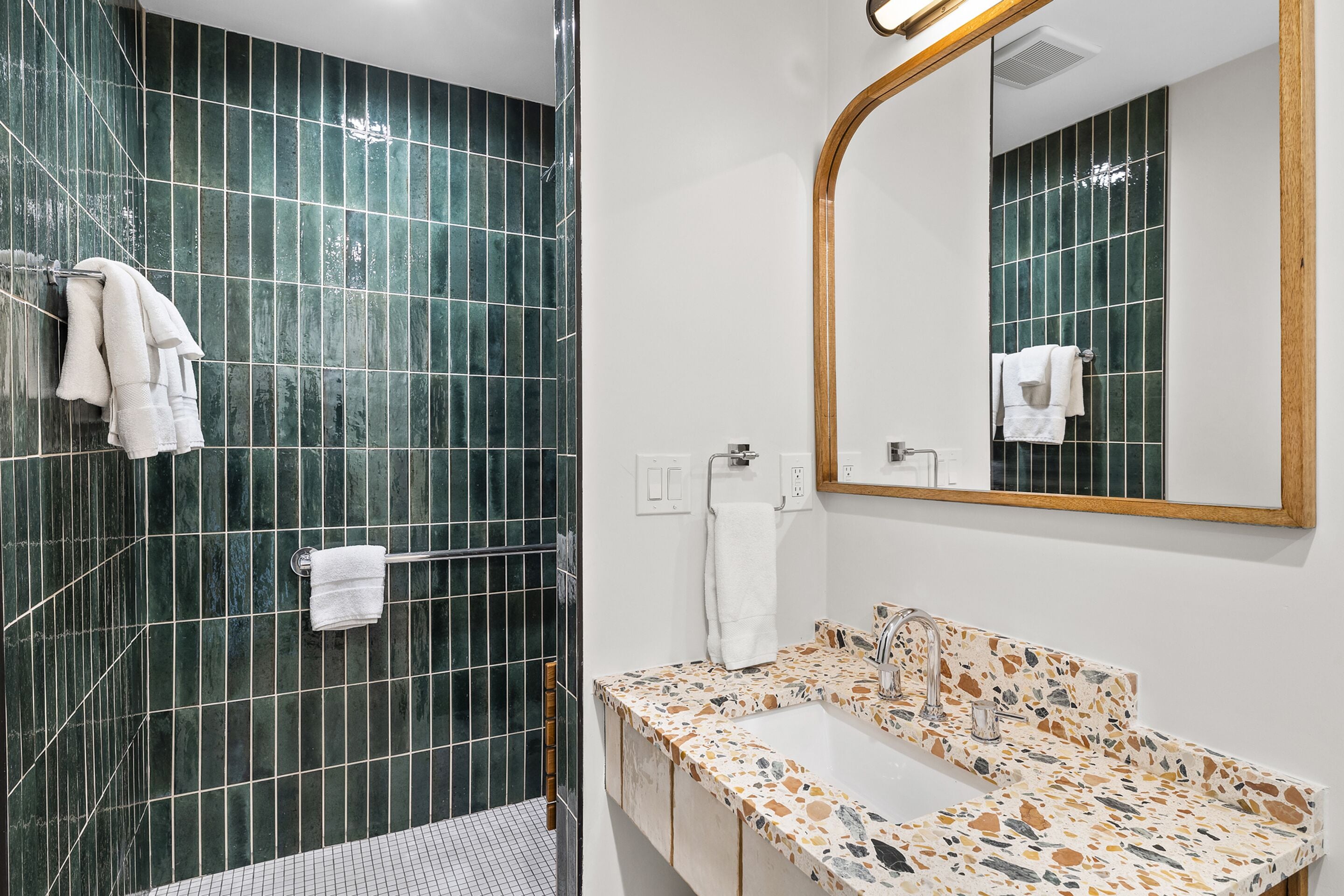 Un bagno con doccia, lavabo con piano in mosaico e specchio con cornice in legno.