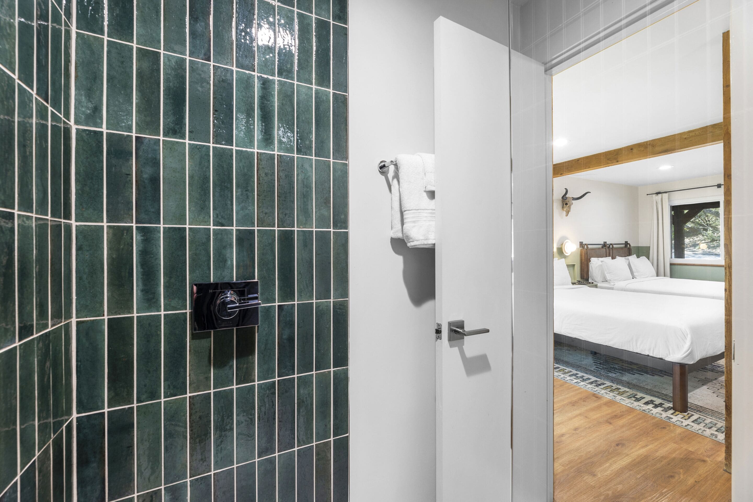 A hotel room with a tiled shower wall, a bed with white linens, and a wooden floor.