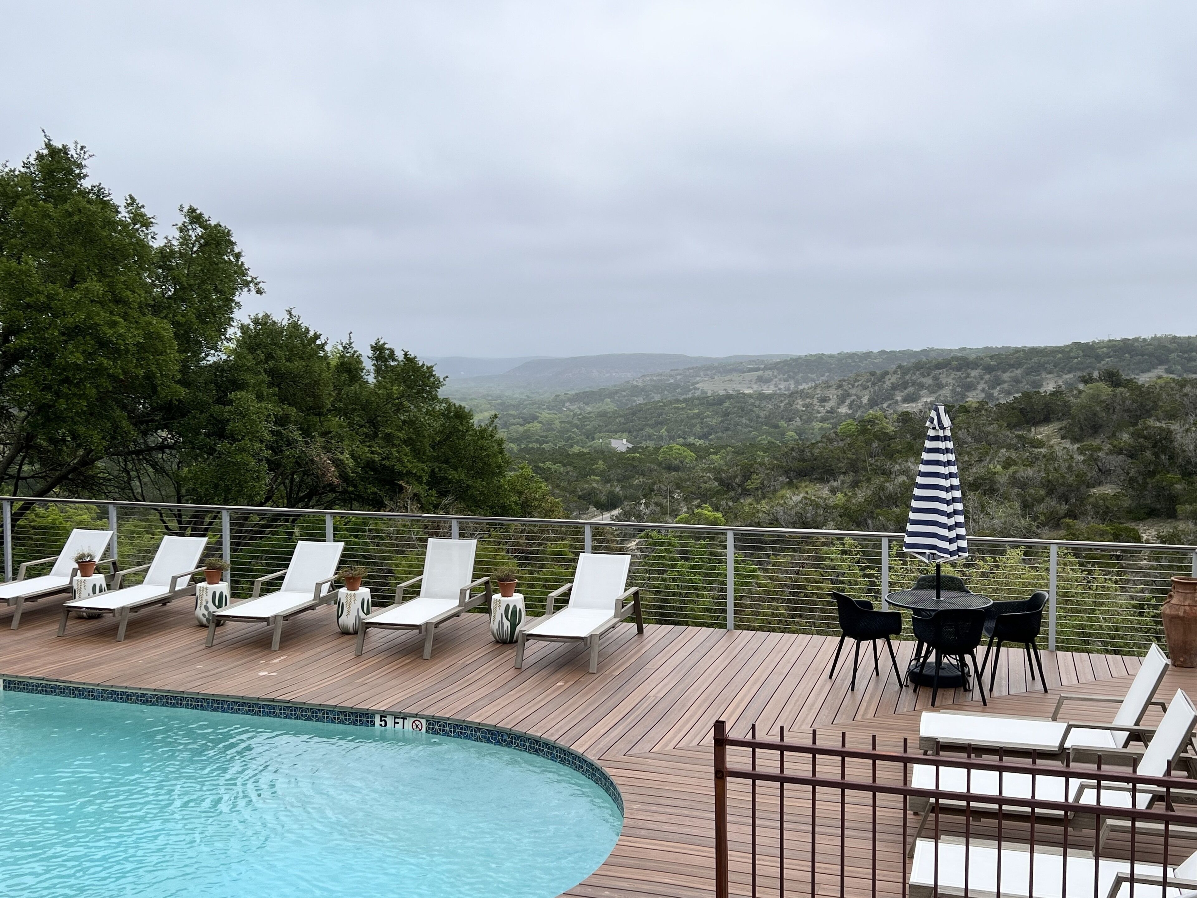 A poolside area with lounge chairs and a table, overlooking a scenic landscape.