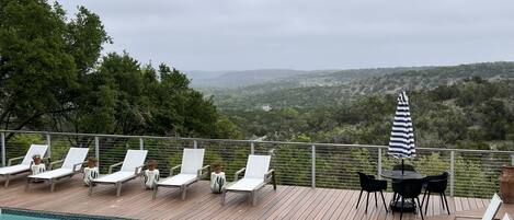 A poolside area with lounge chairs and a table, overlooking a scenic landscape.