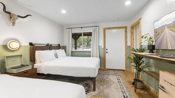 Habitación de hotel con dos camas, un escritorio, una planta y un ventanal grande.