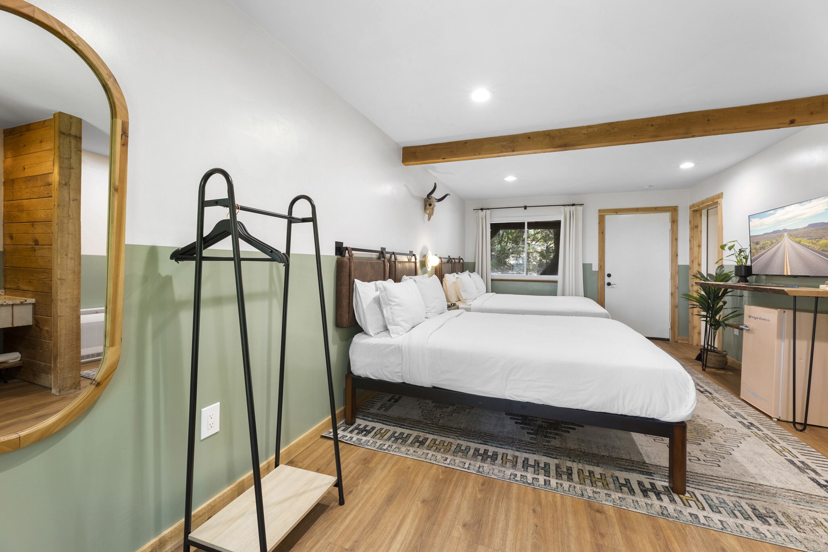 A bedroom with two beds, a wooden ceiling, a mirror, and a mounted animal head.