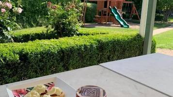 Une table avec une assiette de nourriture et une tasse, le tout placé devant un jardin où se trouve une structure de jeux en bois.