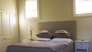 Un dormitorio con cama, mesitas de noche, una lámpara y un ventanal.