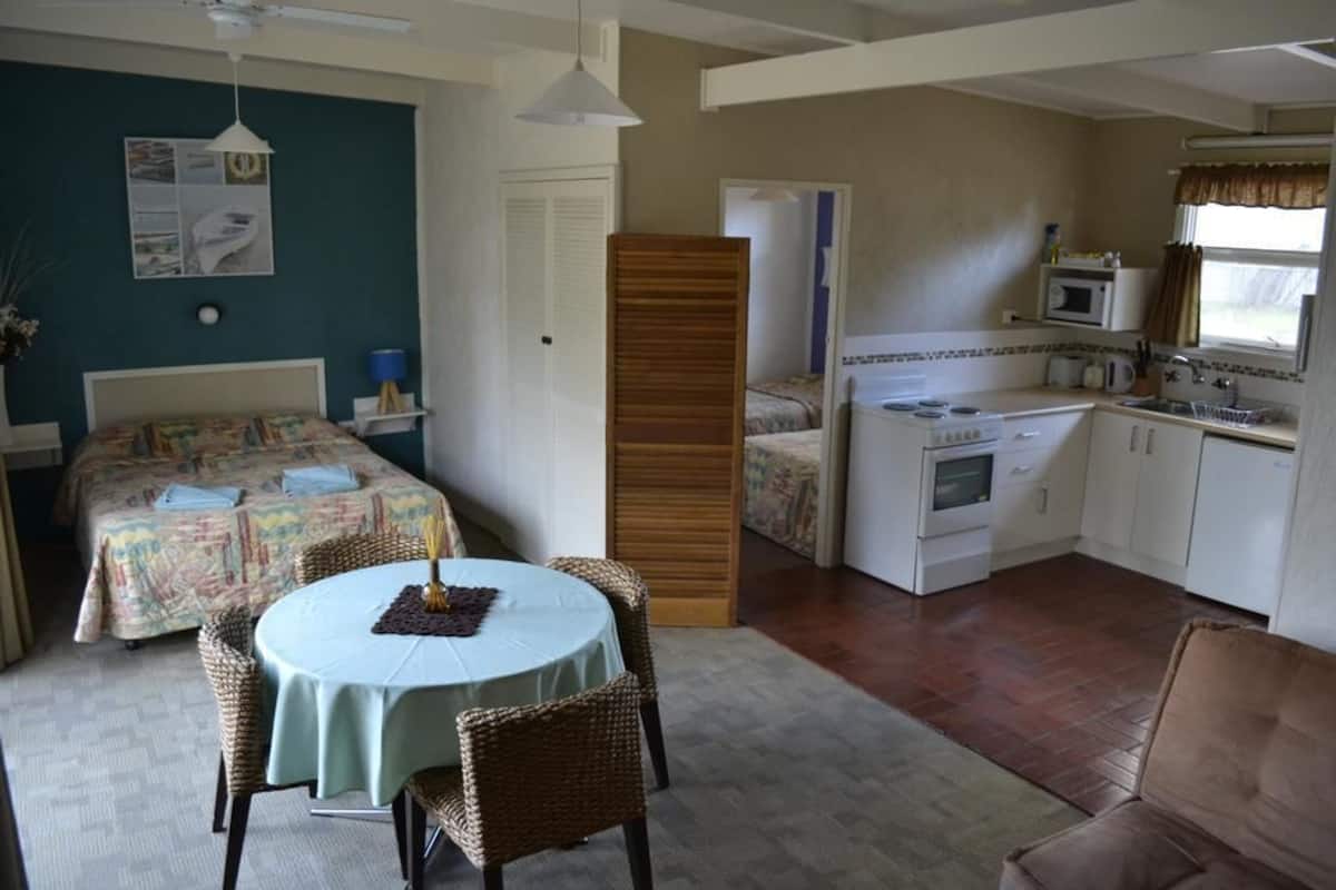 A compact room with a bed, a dining table with chairs, a kitchenette, and a small living area with a sofa.