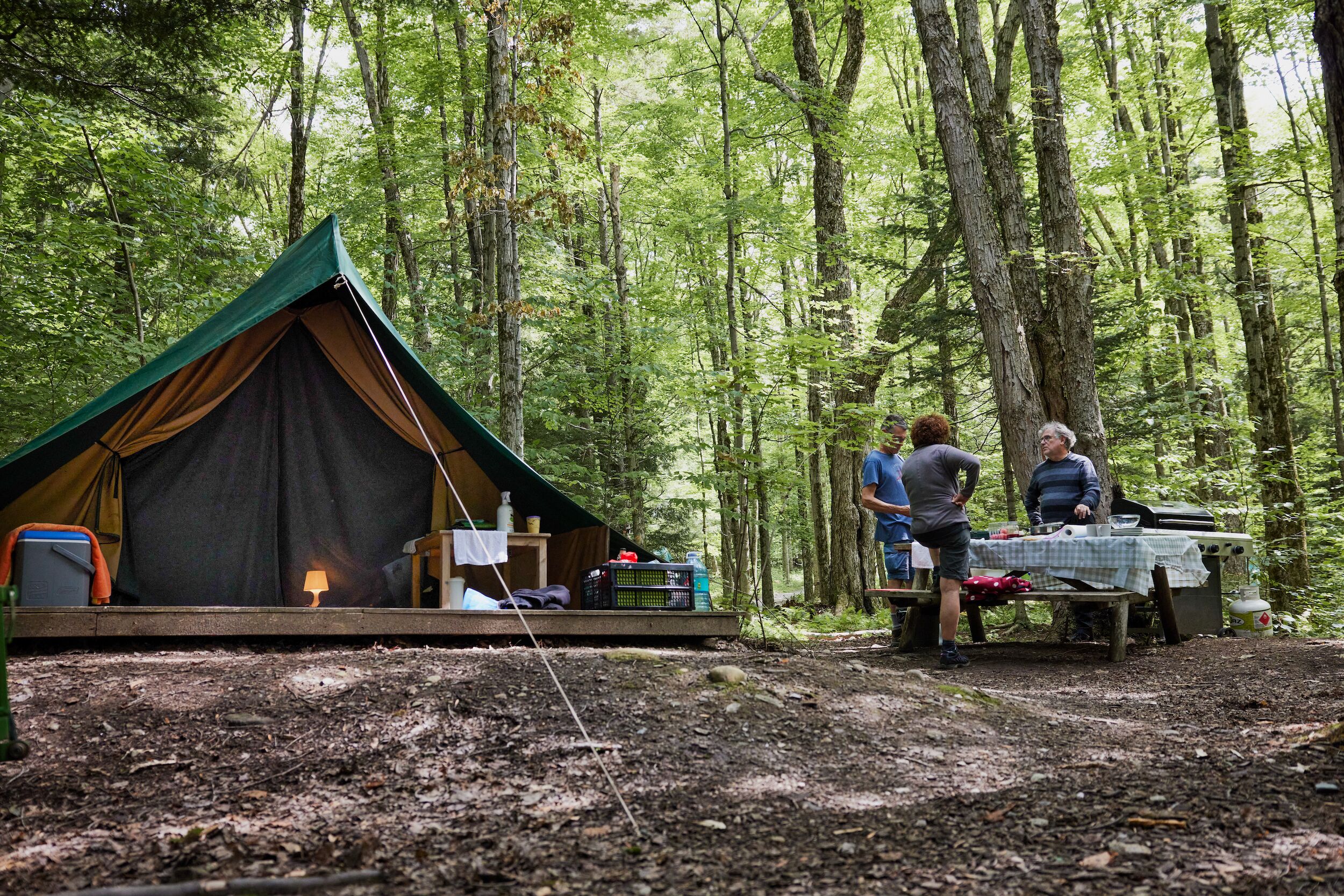 A tent set up in a forest with a table and chairs nearby.