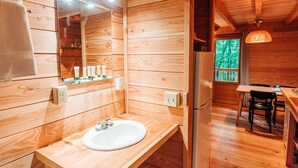 A wooden cabin interior with a wooden sink, mirror, and a dining area with a table and chairs.