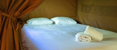A bed with white linens, two pillows, and a rolled towel.